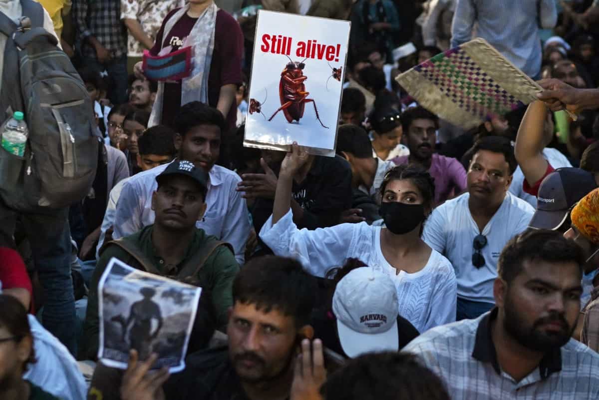 در میان جمعیت معترض یک دختر جوان پلاکاردی با تصویر یک سوسک در دست دارد که روی آن به انگلیسی نوشته شده: «هنوز زنده است».