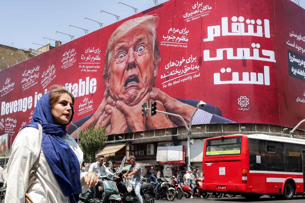 تصویری از یک زن در خیابان جمهوری تهران که از کنار بیلبورد بزرگی با تصویر دونالد ترامپ عبور می‌کند.