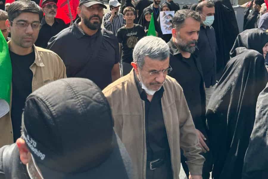 محمود احمدی‌نژاد با کاپشنی بر تن و ماسکی بر چهره در میان عده‌ای دیده می‌شود.