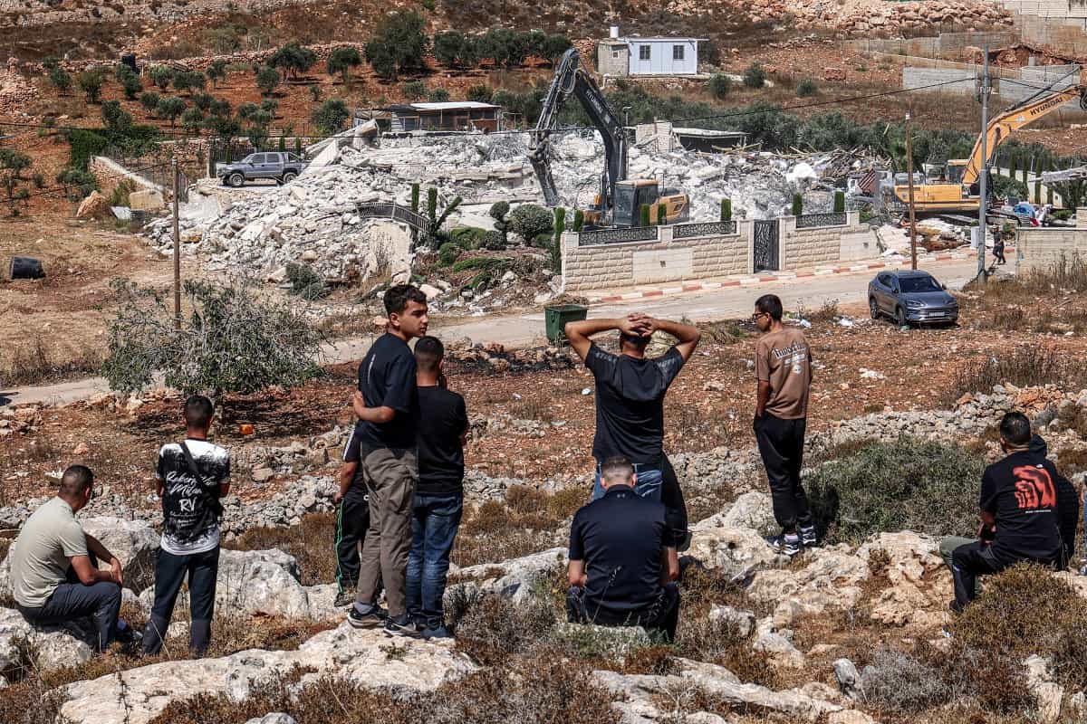 چند فلسطینی از دور شاهد تخریب یک ساختمان توسط بولدوزرهای اسرائیلی هستند.