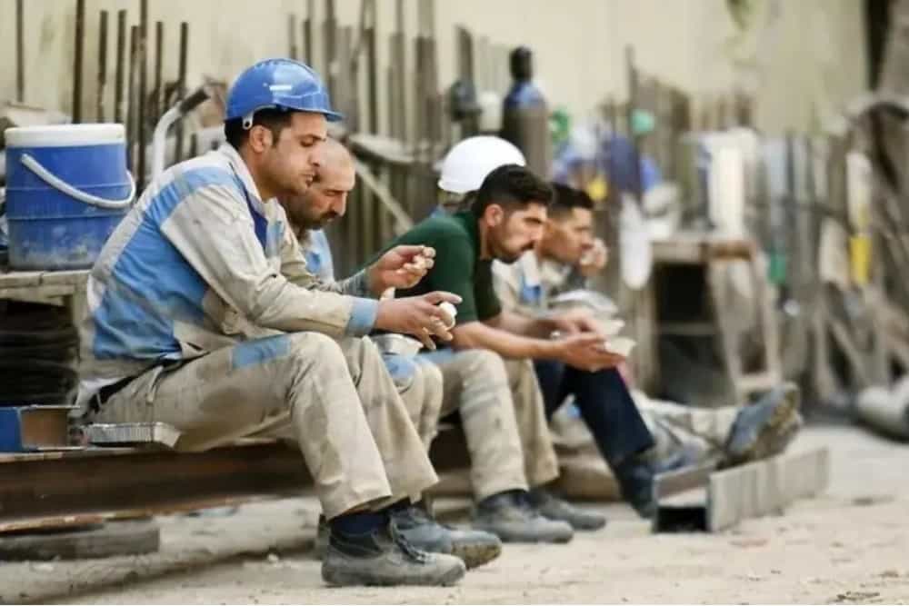 چند کارگر در محل کار خود نشسته‌اند و لقمه غذای خود را می‌خورند.