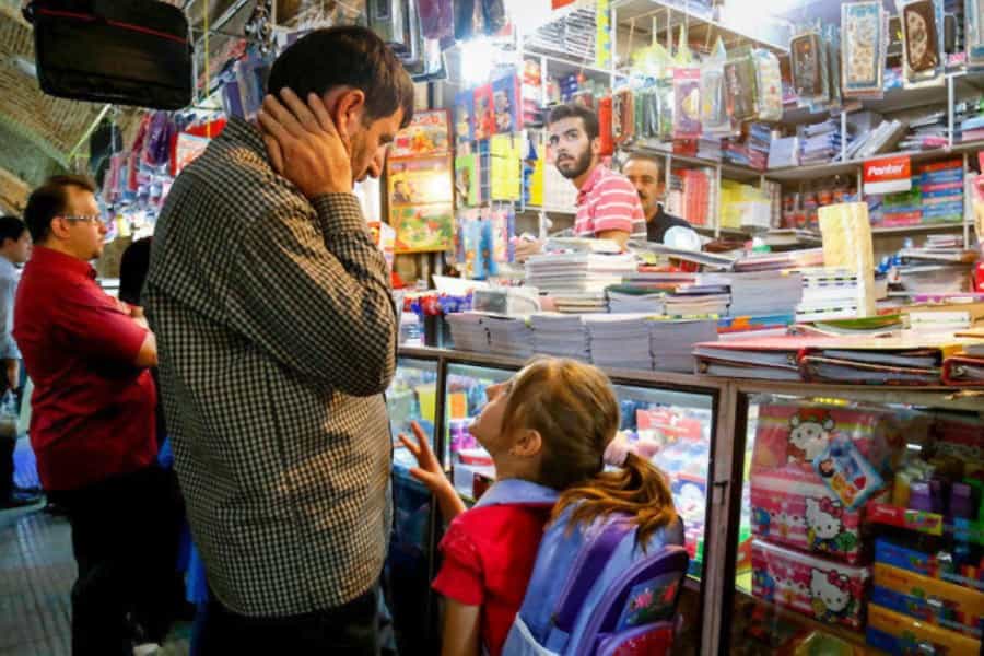 مردی با دخترش جلوی یک مغازه فروش نوشت‌افزار ایستاده و با اجناس نگاه می‌کند. دخترش به او چیزی می‌گوید.
