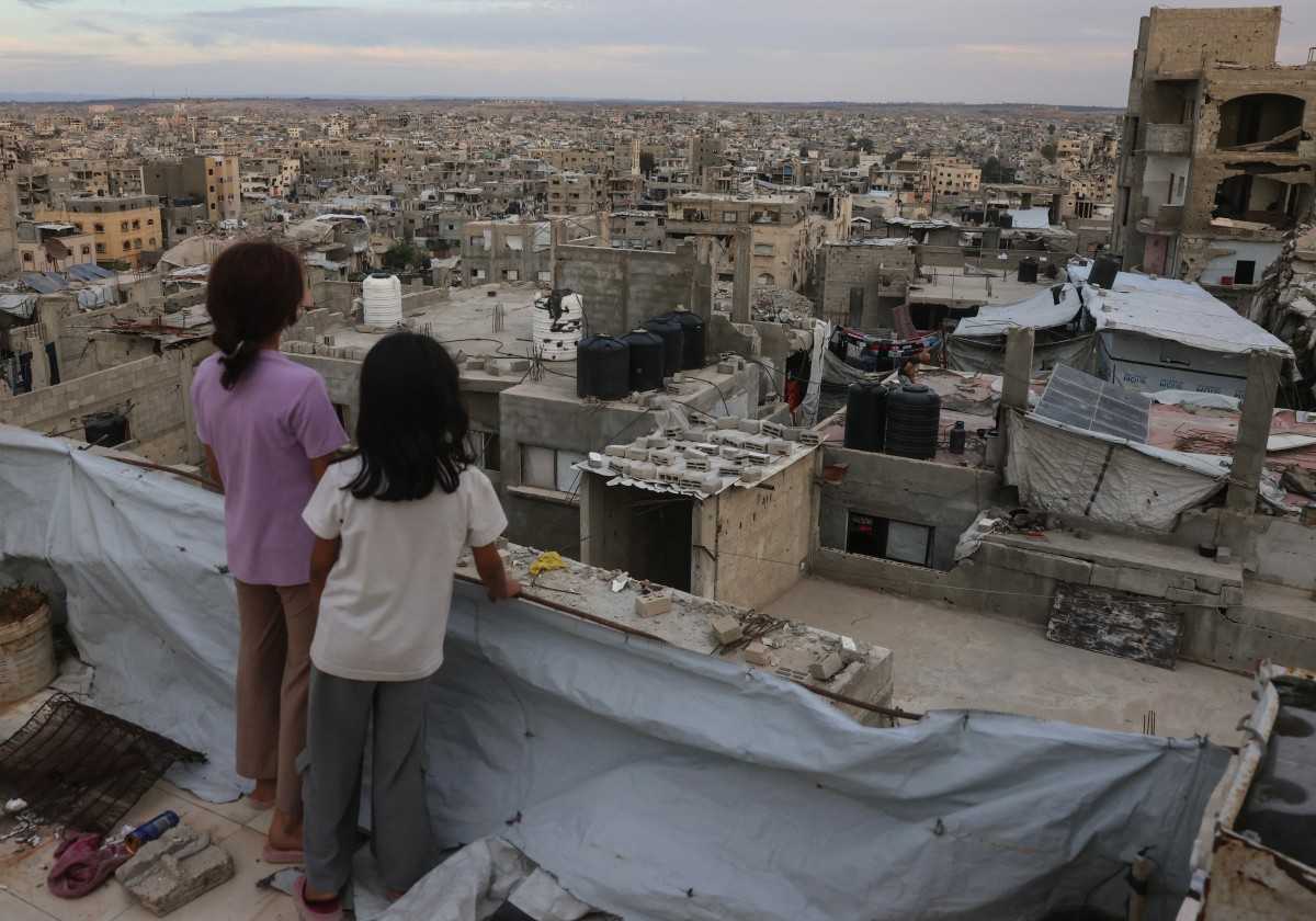 دو کودک فلسطینی بر روی پشتبام ساختمانی در اردوگاه پناهجویان جبالیا در شمال نوار غزه ایستادهاند و از بالا به منظره ویران شهر نگاه میکنند.