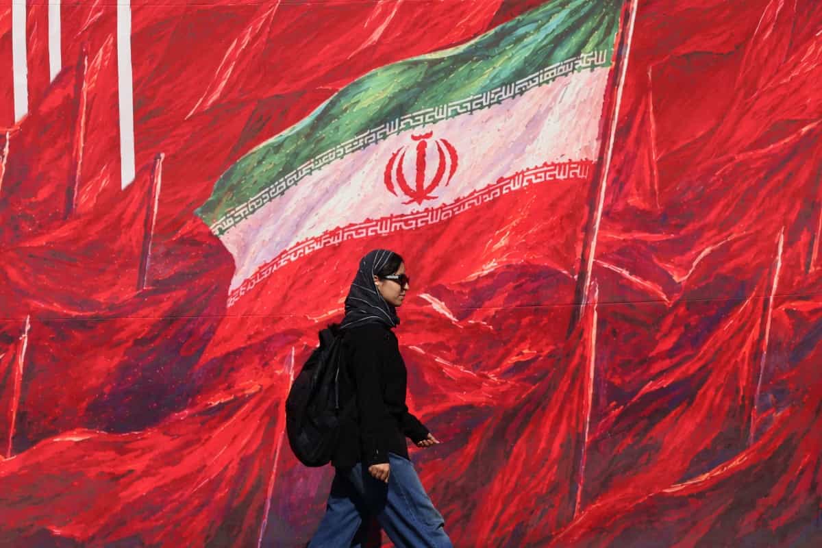 زنی در تهران از کنار دیوارنگاره‌ای می‌گذرد که در آن پرچم جمهوری اسلامی در میان ده‌ها پرچم سرخ رنگ دیده می‌شود.