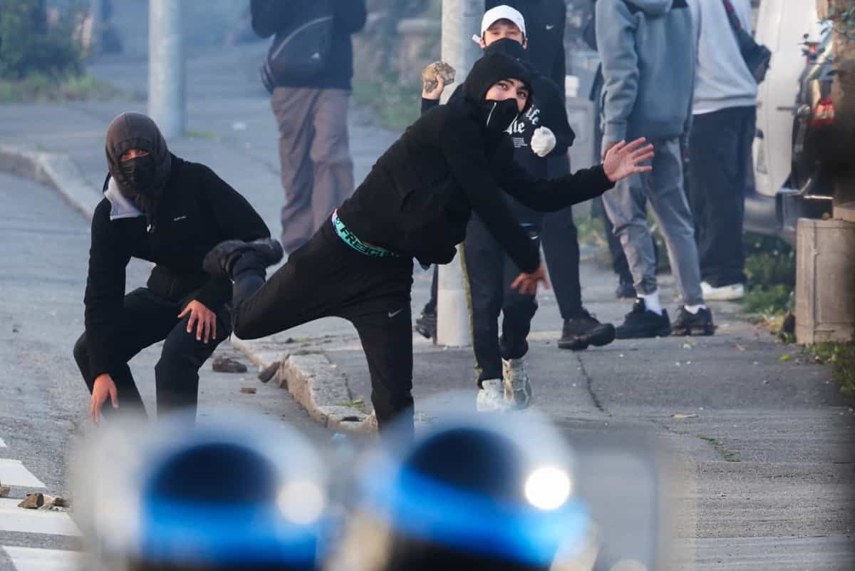 دانش‌آموزان معترض با چهره‌های پوشیده، به سوی مأموران امنیتی سنگ پرتاب می‌کنند.